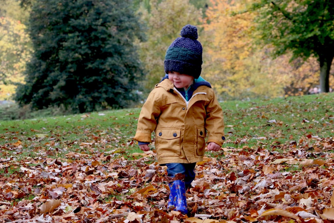 Bretton, Peterborough: boy wearing orange bubble jacket walking on dry fallen leaves on ground
